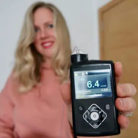 A blonde woman holding out a Medtronic insulin pump