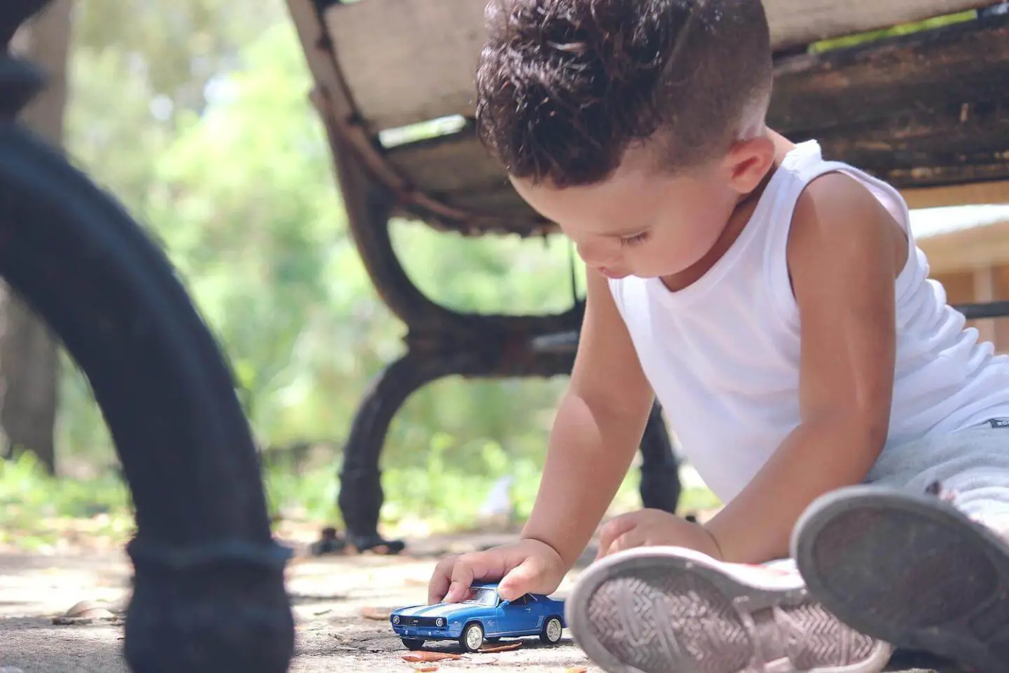 A toddler sitting on the floor pushing a blue toy car around