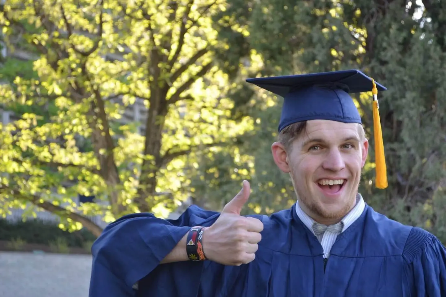 A man in a blue cap and gown giving a thumbs up