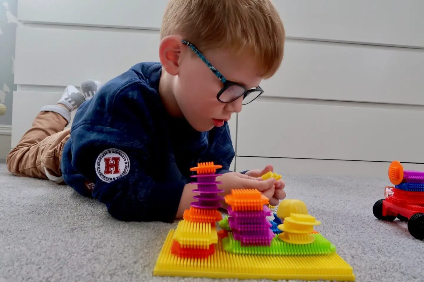 A boy is lying on the ground playing with Stickle Bricks