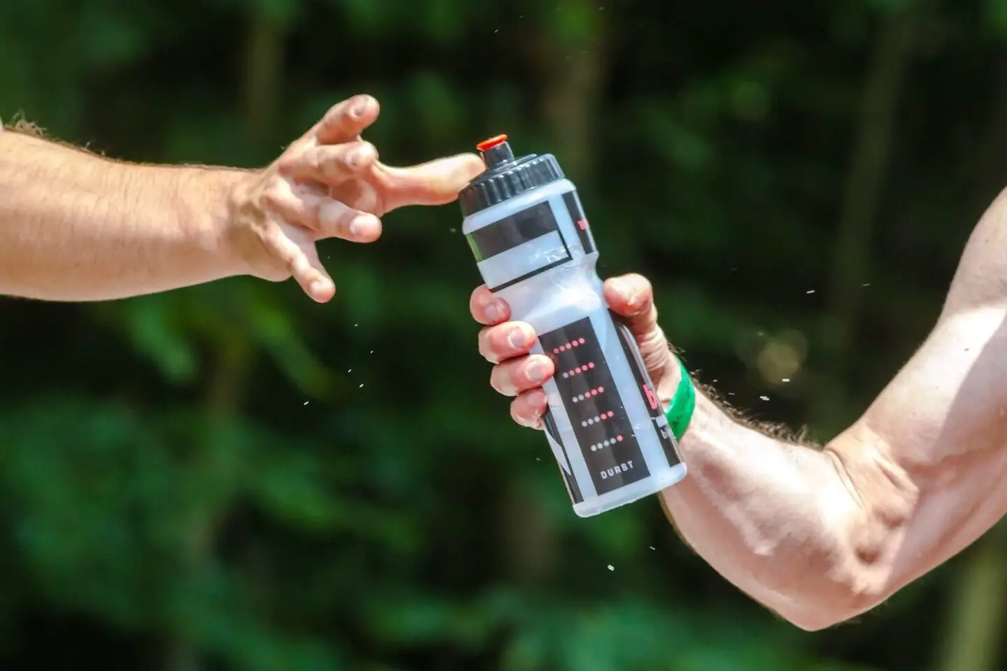 A mans arm holding out a water bottle. Another arm reaches out to take it.
