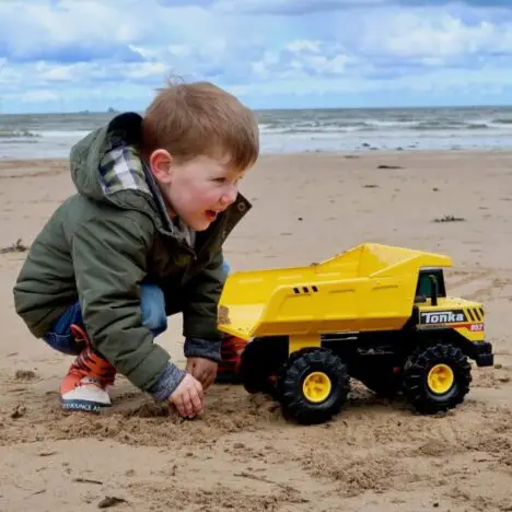 A child on the beach playing with a yellow Tonka dump truck