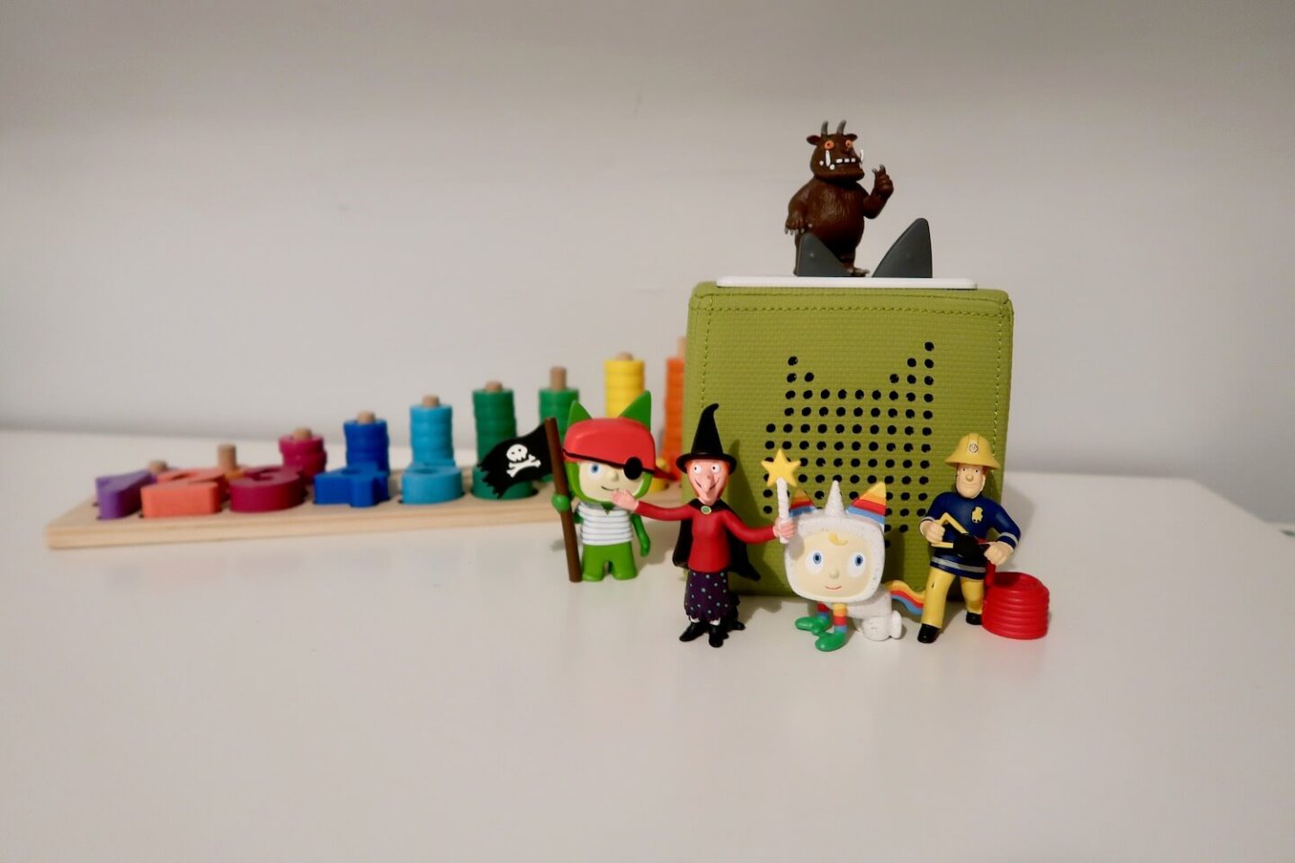 A green Tonie box. A Gruffalo Tonie character is on the top, and a pirate, witch, unicorn and fireman are sitting in front.