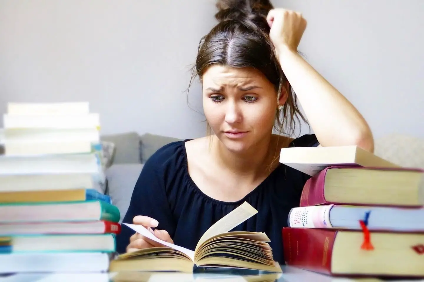 A woman sitting at a table with stacks of books. She looks frazzled as he looks at one of them