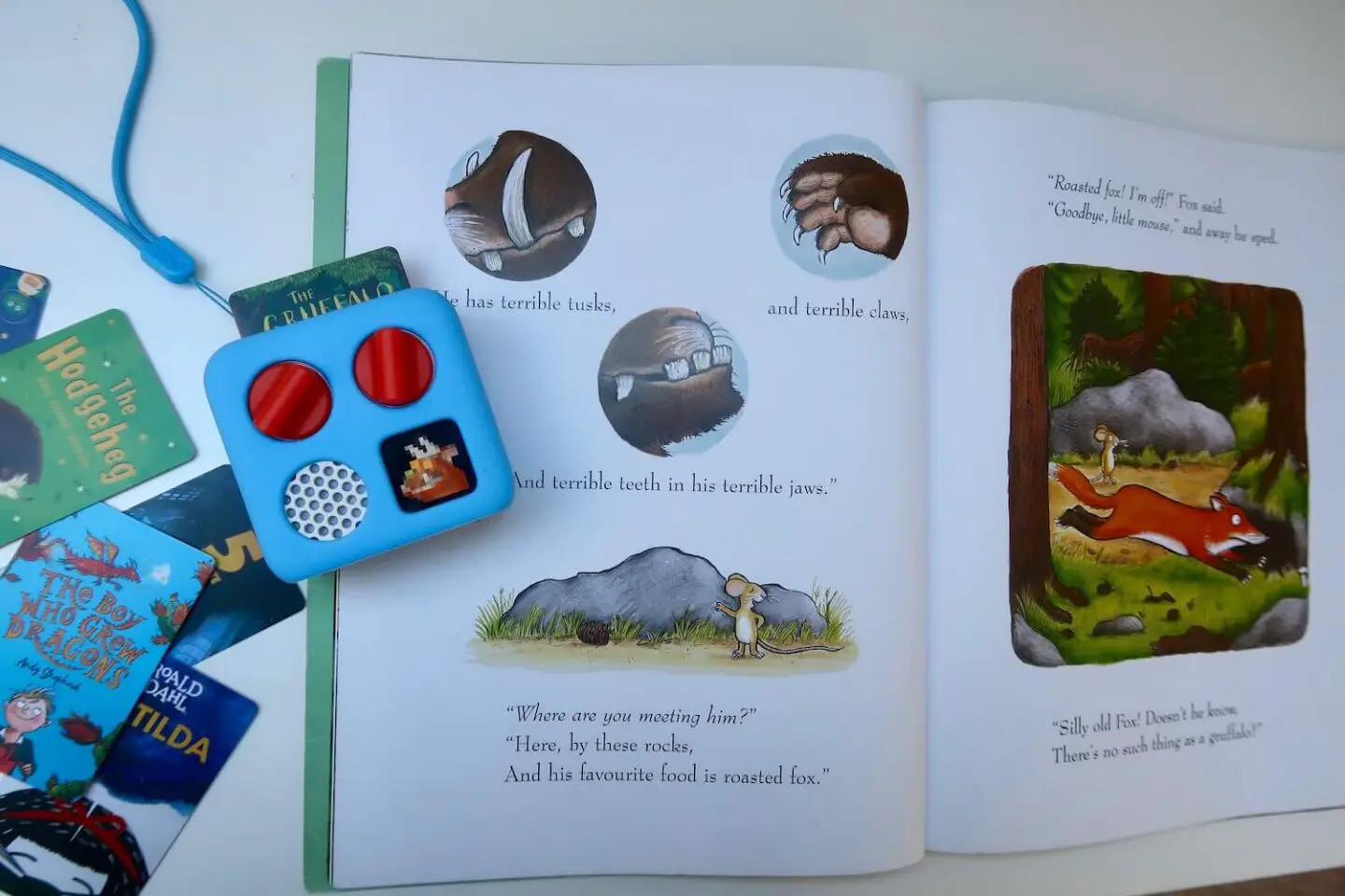 The Gruffalo booking lying open. A Yoto mini player is sitting on the edge of a page with the Gruffalo audiobook card in it. Additional Yoto cards are sitting to the left of the book.
