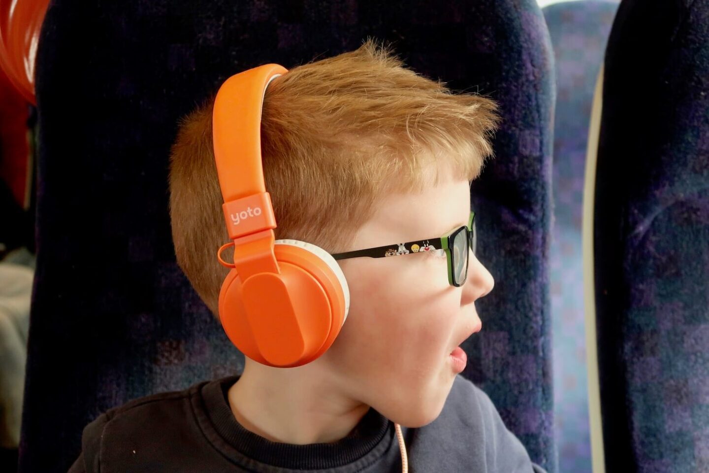 A boy with orange Yoto headphones on looking to the side with a look of amazement on his face
