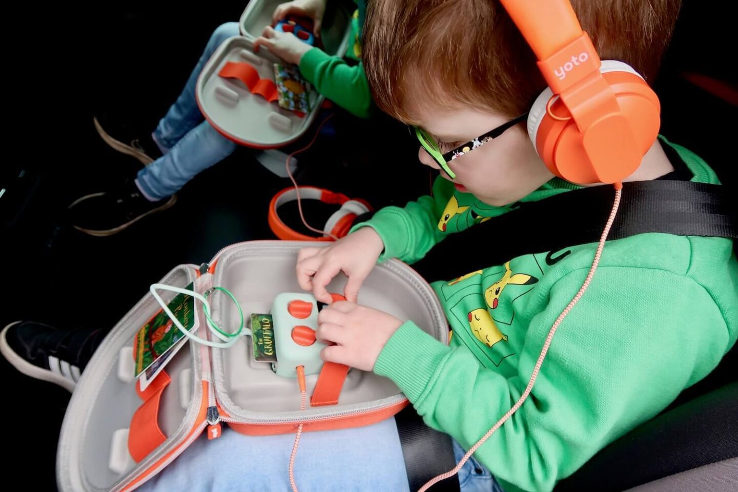 A boy wearing orange headphone and touching his yoto mini. It has a Gruffalo card in the player.