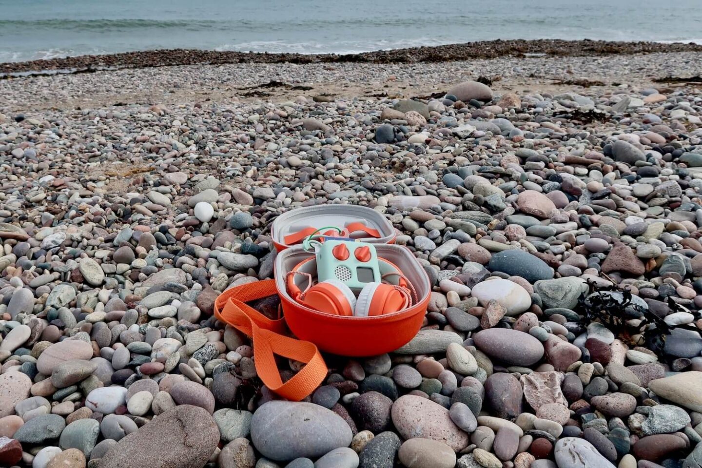 A yoto mini travel case open on a stone beach. The sea can be seen in the background.