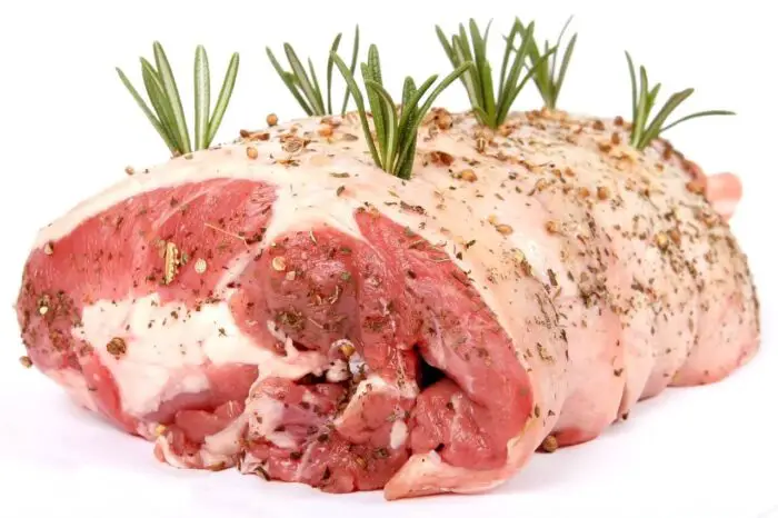 A raw lamb joint with rosemary stuffed into it, waiting to be roasted.