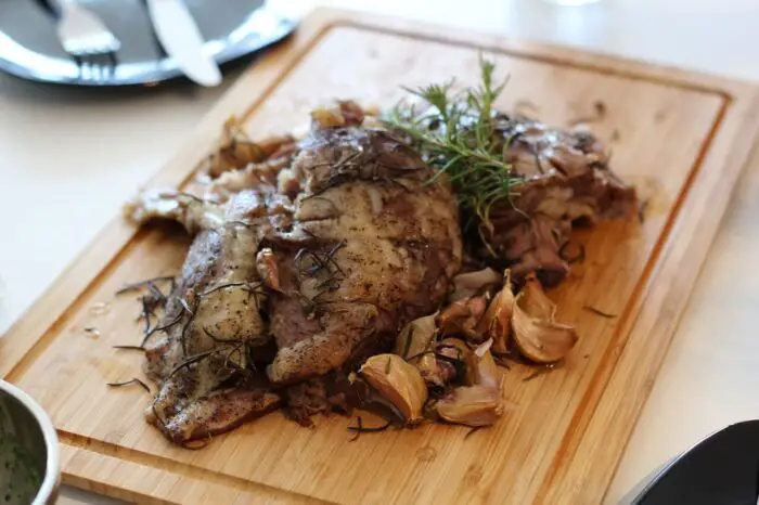 A roast joint of lamb on a wooden board, with rosemary and garlic