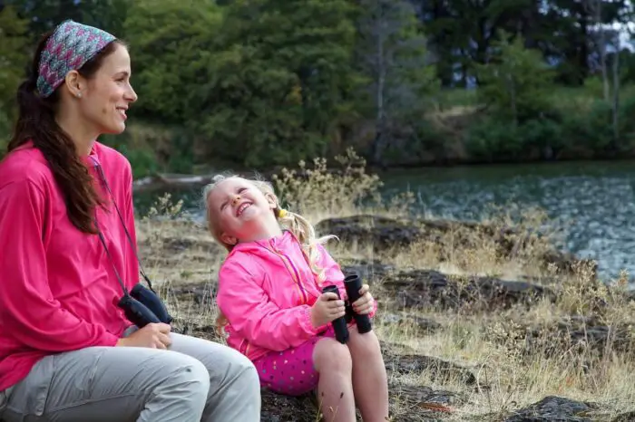 A woman and a little girl are sitting outside. The both have on bright pink tops and are holding binoculars